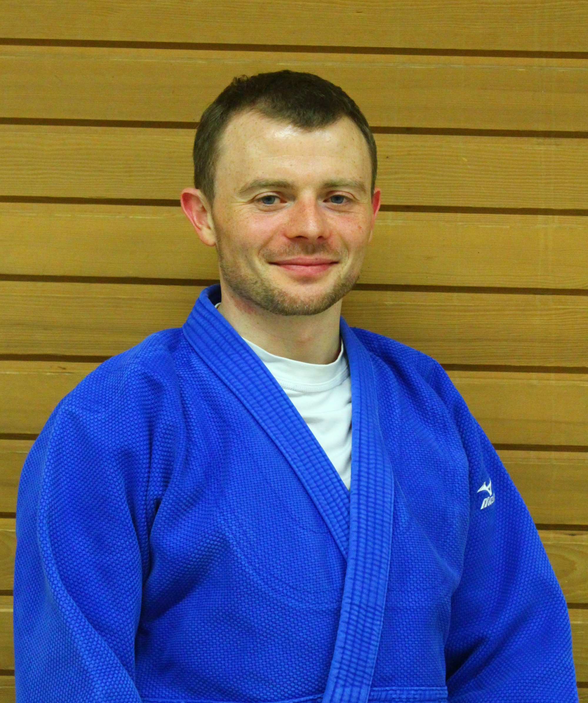Porträ von Florian Braun, im Blauen Judo Anzug vor einer Holzwand.